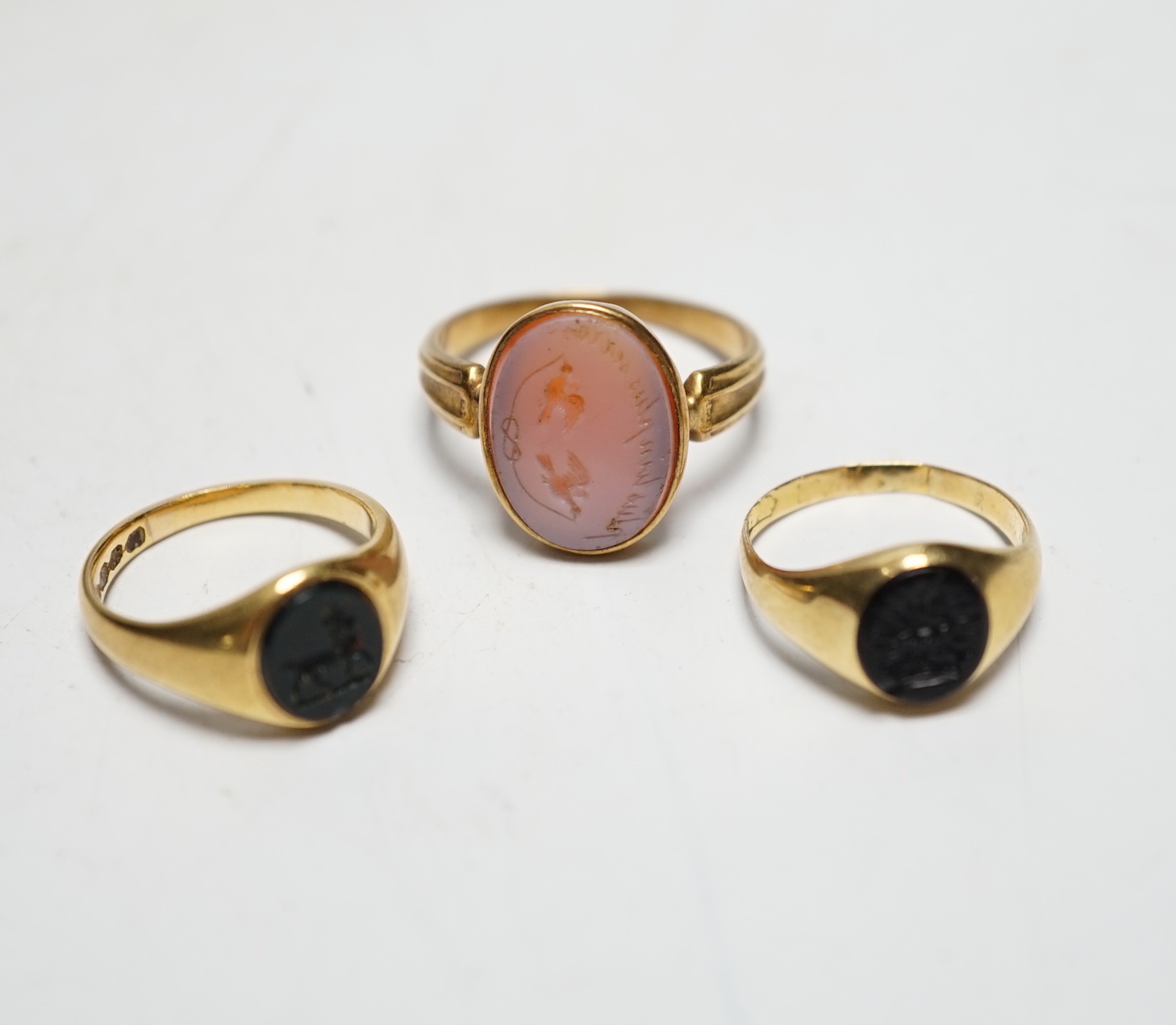 A Victorian yellow metal and sardonyx set oval seal ring, the matrix carved with two birds and motto, size O, together with two early 20th century yellow metal and chalcedony set child's signet rings, gross weight 9.7 gr